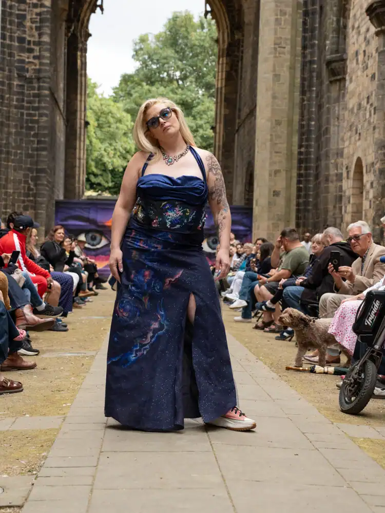 A model walks the catwalk in a navy halter dress with a floral bodice and a starry skirt with a thigh split.