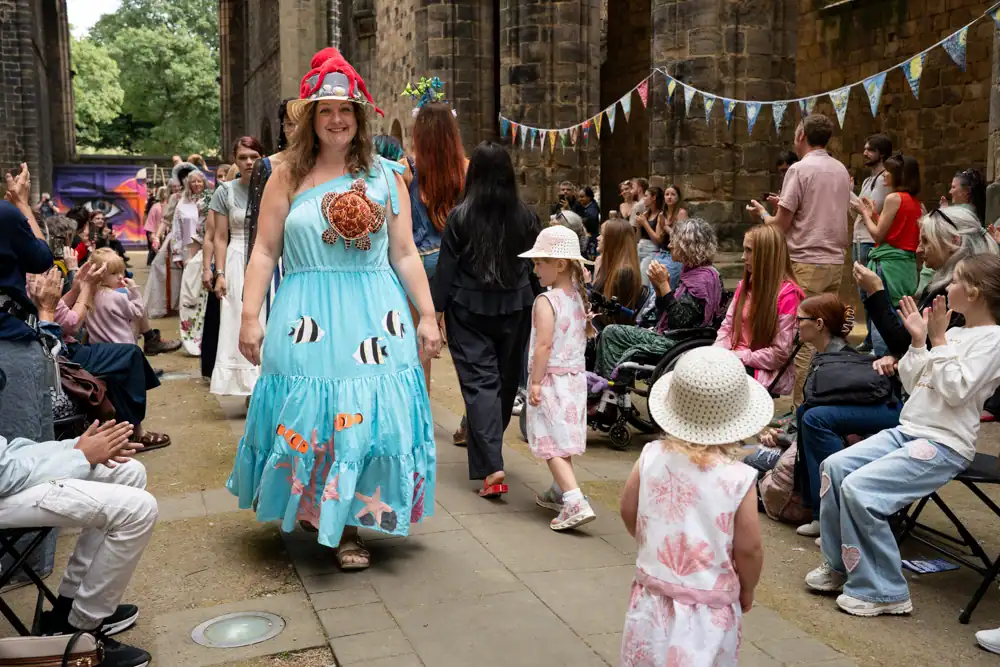 A model walks in a pale blue dress appliquéd with a turtle, fish, and starfish, wearing a straw hat topped with a red toy octopus.
