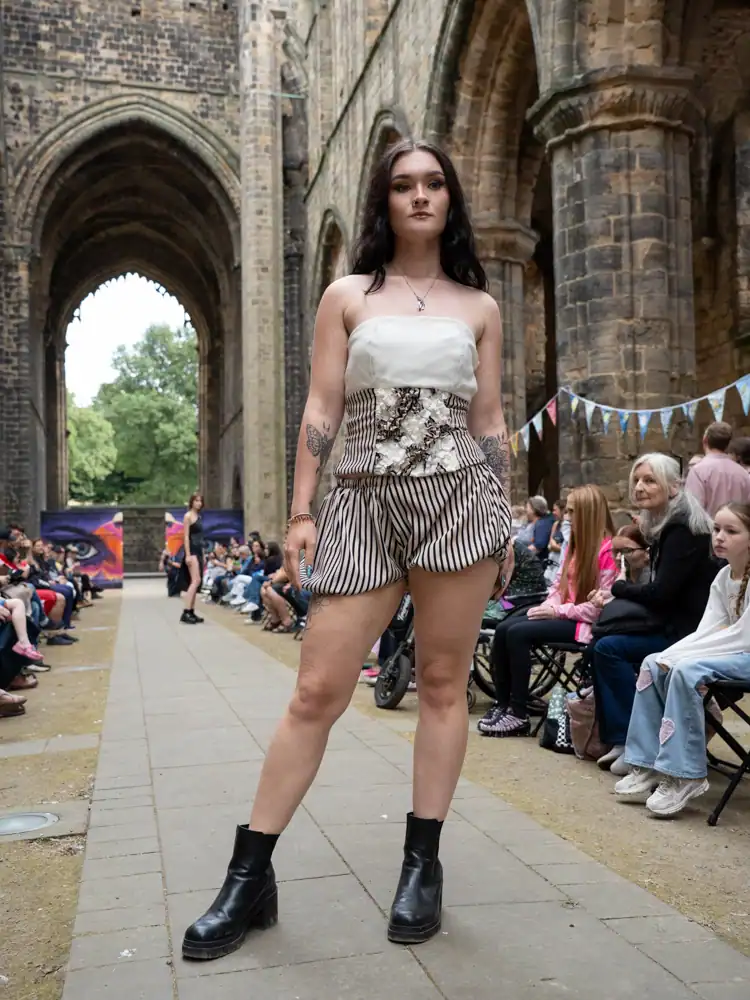 A model stands wearing a white strapless top with floral embellishment and black-and-white striped shorts.