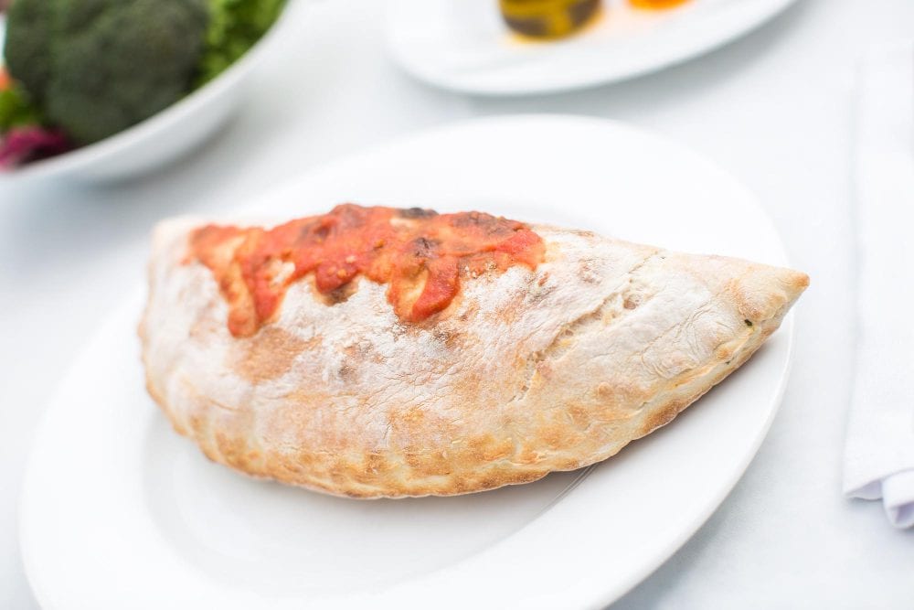 Traditional Italian calzone pizza with tomato sauce on a white plate, ideal for catering and takeaway.