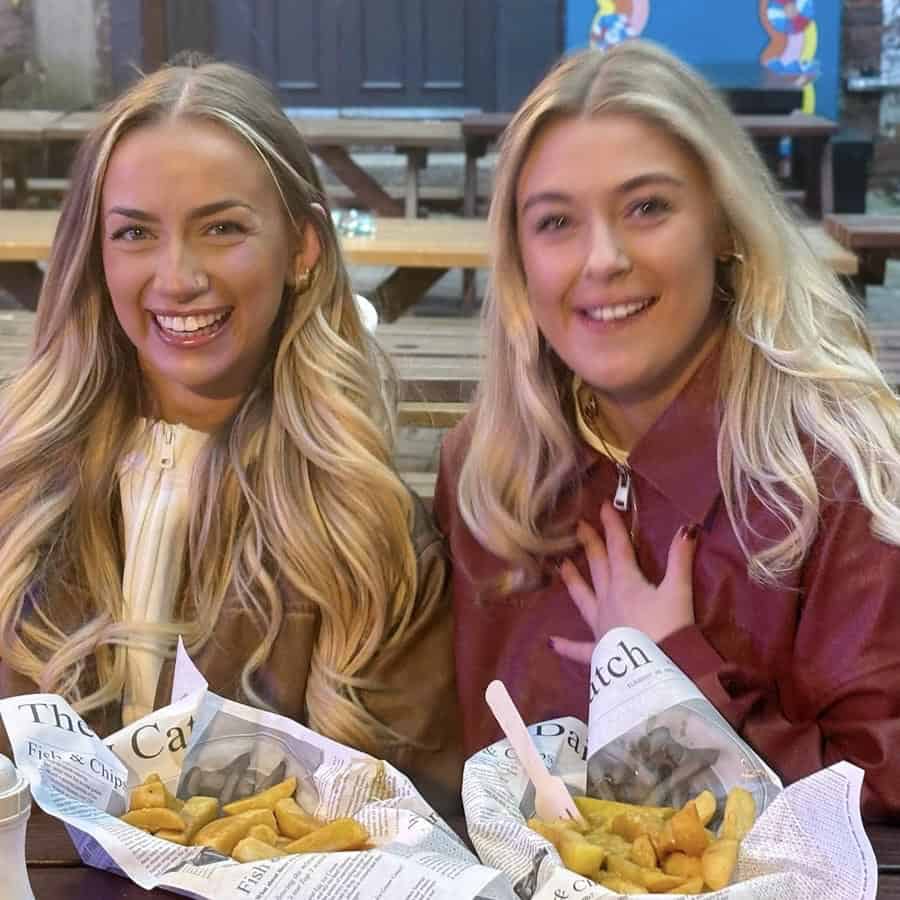 Smiling young women enjoying fish and chips at an outdoor dining area in the UK.