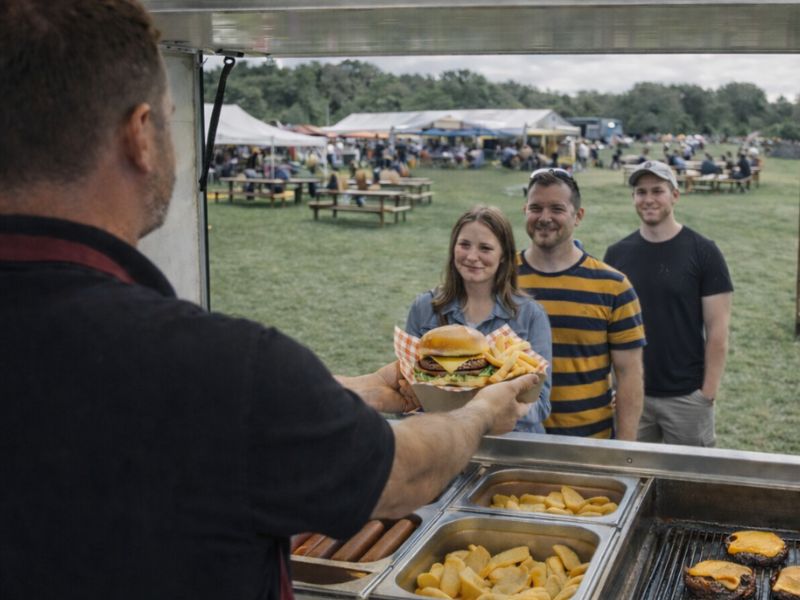 Freshly prepared burgers served at outdoor catering event in a park setting.