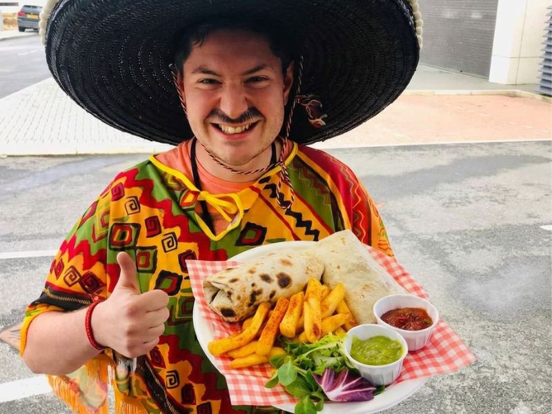 KK Catering Customer holding a tray of Mexican burrito, fries, and salsa outdoors.