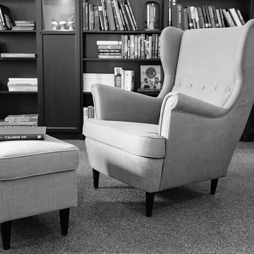 Butik stilleben af lænestol og bogreol, ideelt til afslapning og hyggelige stunder.