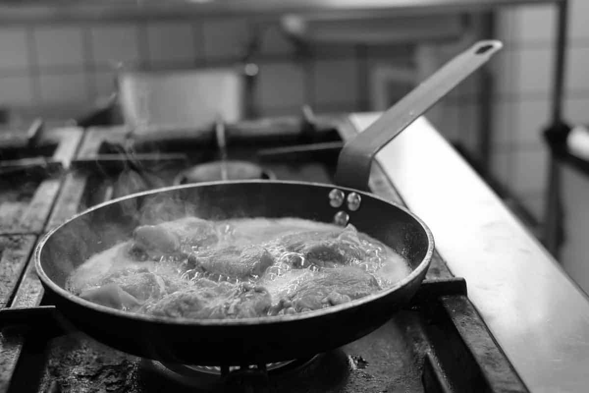 Skarp sort-hvid foto af madlavning i køkkenet, med en pande med kogende mad.