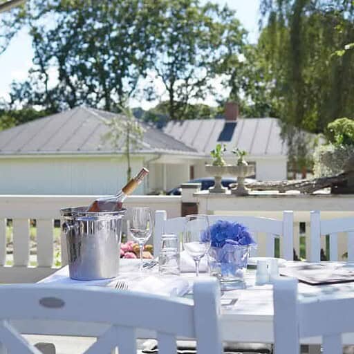Solrig terrasse med udendørs spisning og blomsterdekorationer ved Knudhule Badehotel.