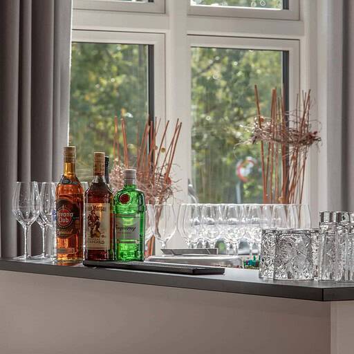 Lysbilledægge med drinks og glas foran et vindue på Knudhule Badehotel. Elegant og stemningsfuldt indrettet hotelbar.