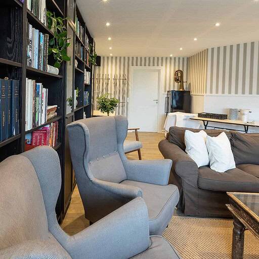 Bogreol med bøger, hyggelig stue på Knudhule Badehotel med komfortable siddemøbler.