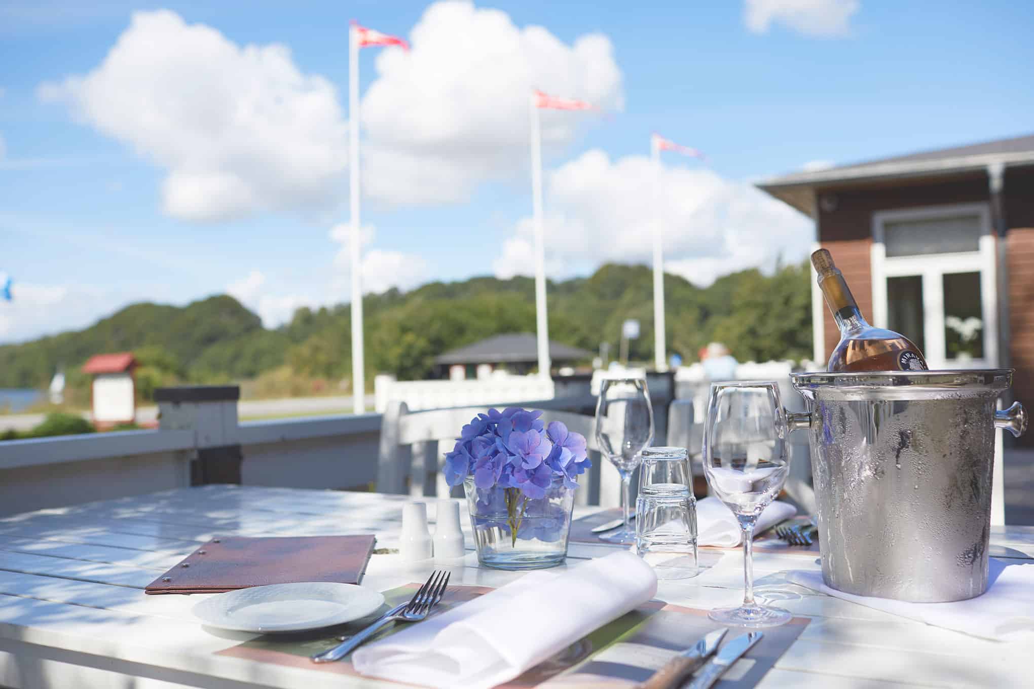 Siddende bord med blomster, vin og glas udenfor ved Knudhule Badehotel, smuk natur og havudsigt.