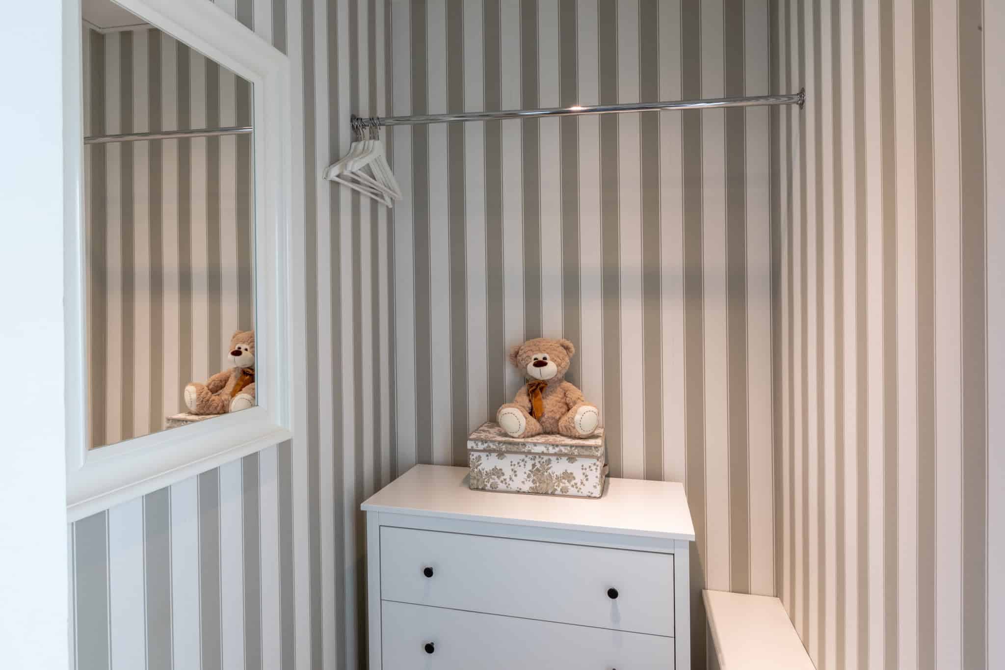 Badeværelse med stribet væg, spejl og tøjdyr i hyggeligt badehotel.