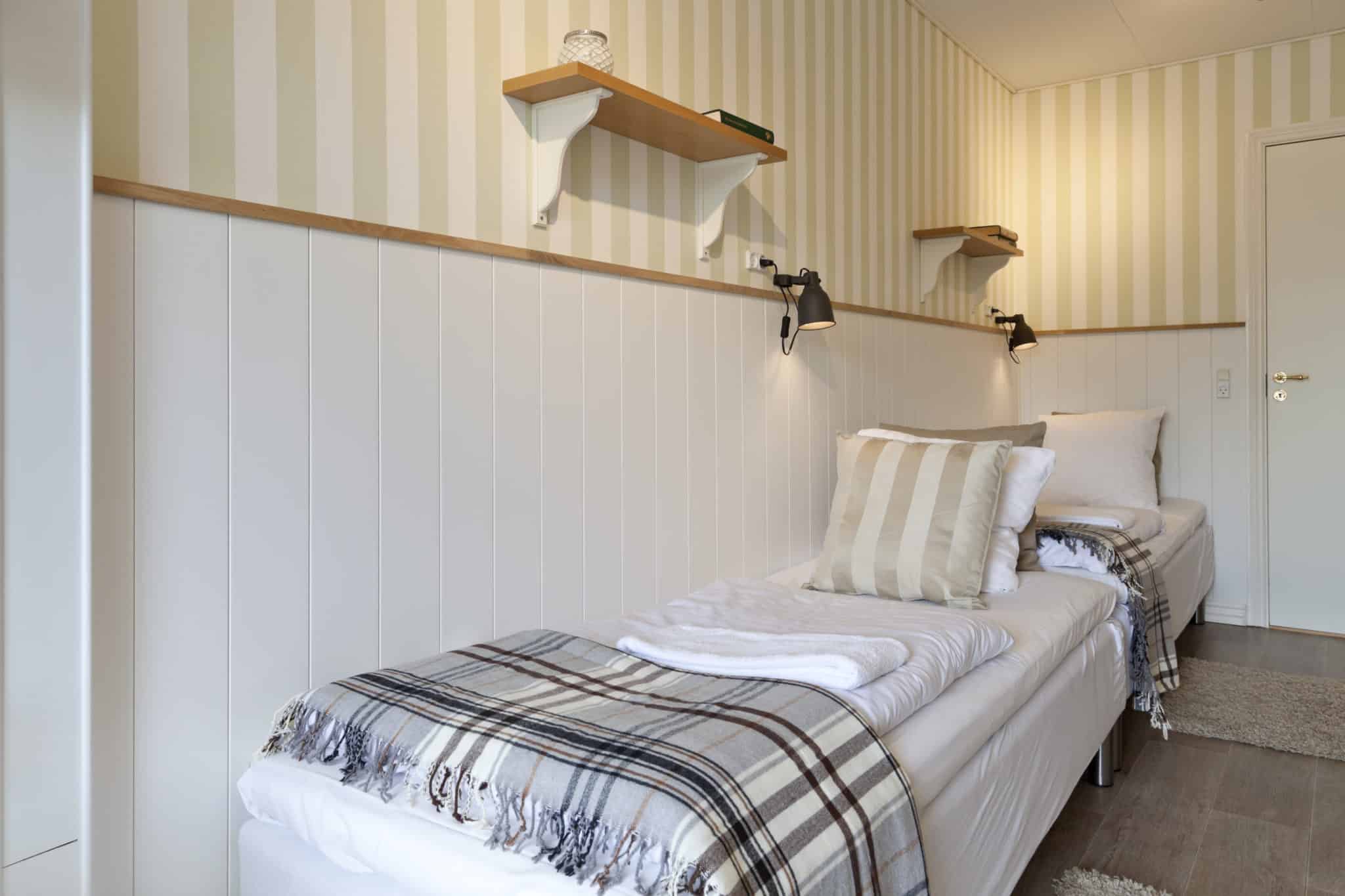 Senge i badehotelværelse med stribede puffer og væglamper, hyggeligt og minimalistisk design.