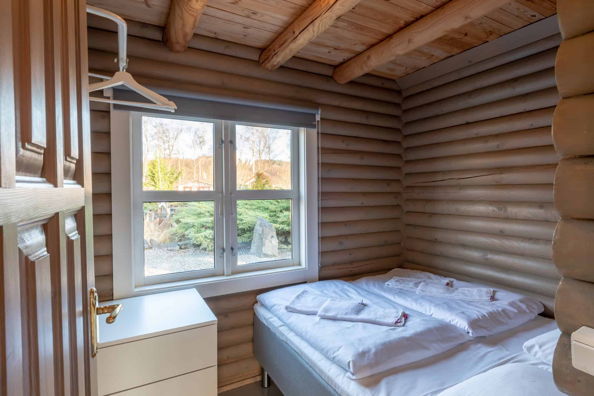 Hytte indretning med trævægge, seng og stor vindue med udsigt til naturen.