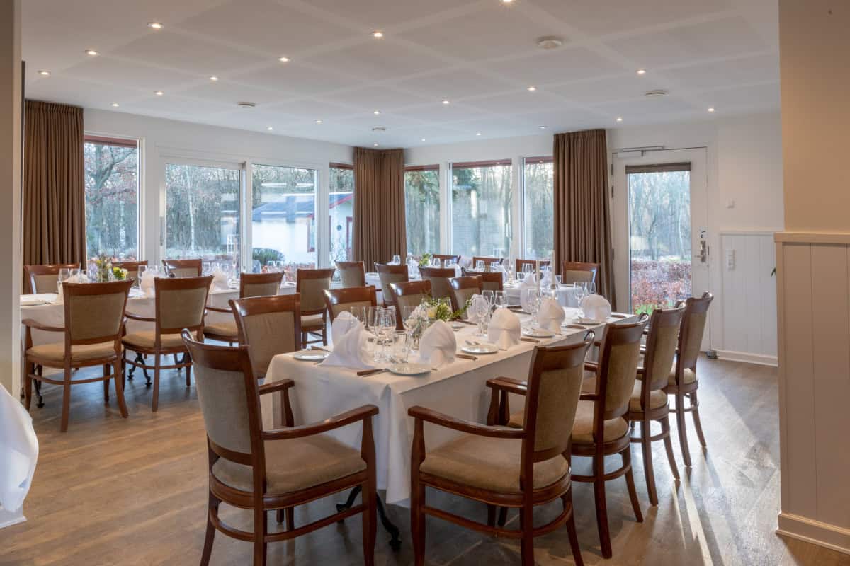 Lyst og elegant spisestue med store vinduer ved Knudhule Badehotel, perfekt til arrangementer.
