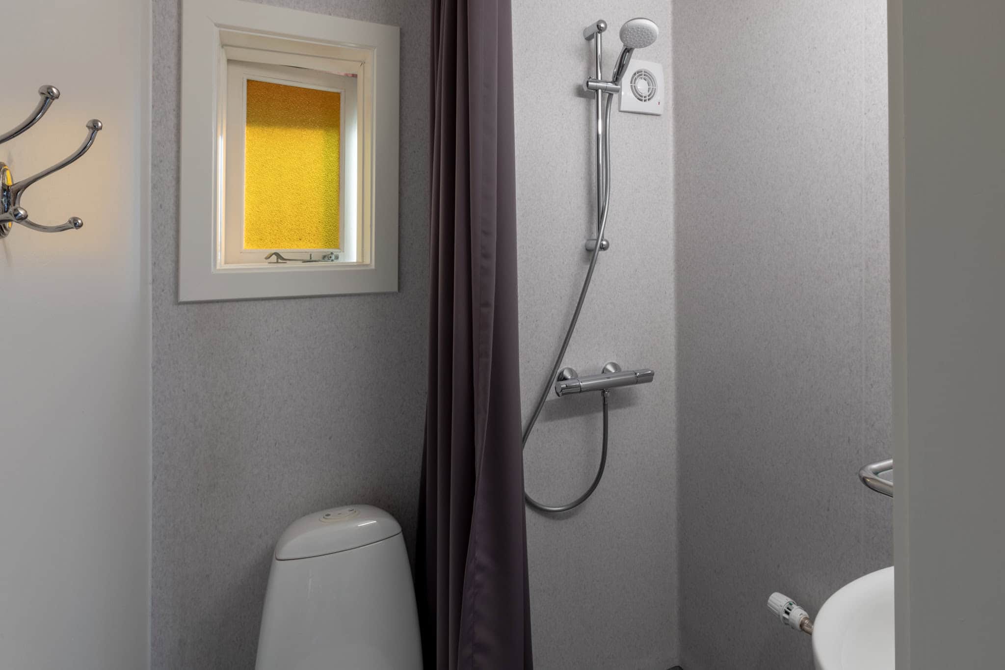 Rustik badeværelsesindretning med bruser, toilet og lille vindue på Knudhule Badehotel.