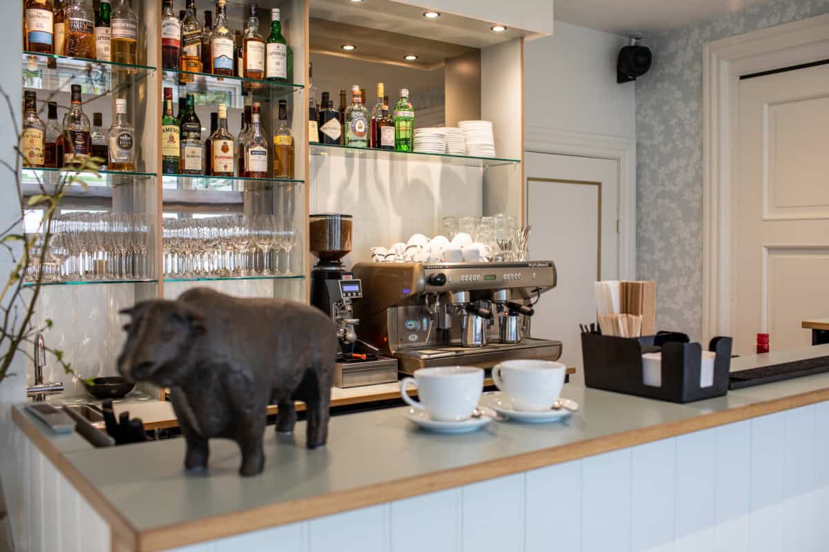 Billed af en bar med kaffemaskine, glas, alkoholiske drikke og dekorative elementer på Knudhule Badehotel.