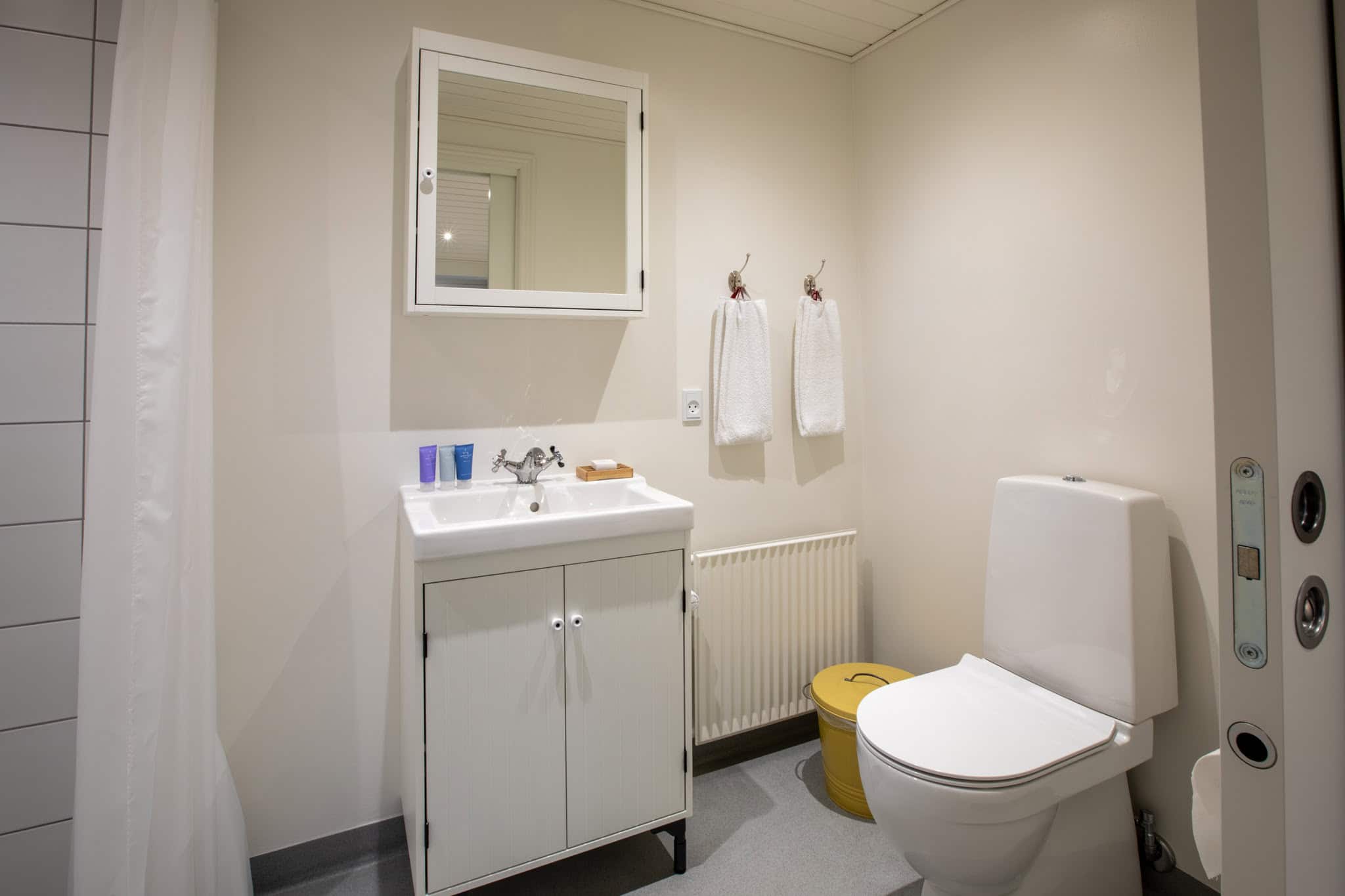 Lyst badeværelse med hvid håndvask, spejlskab og toilet på Knudhule Badehotel.