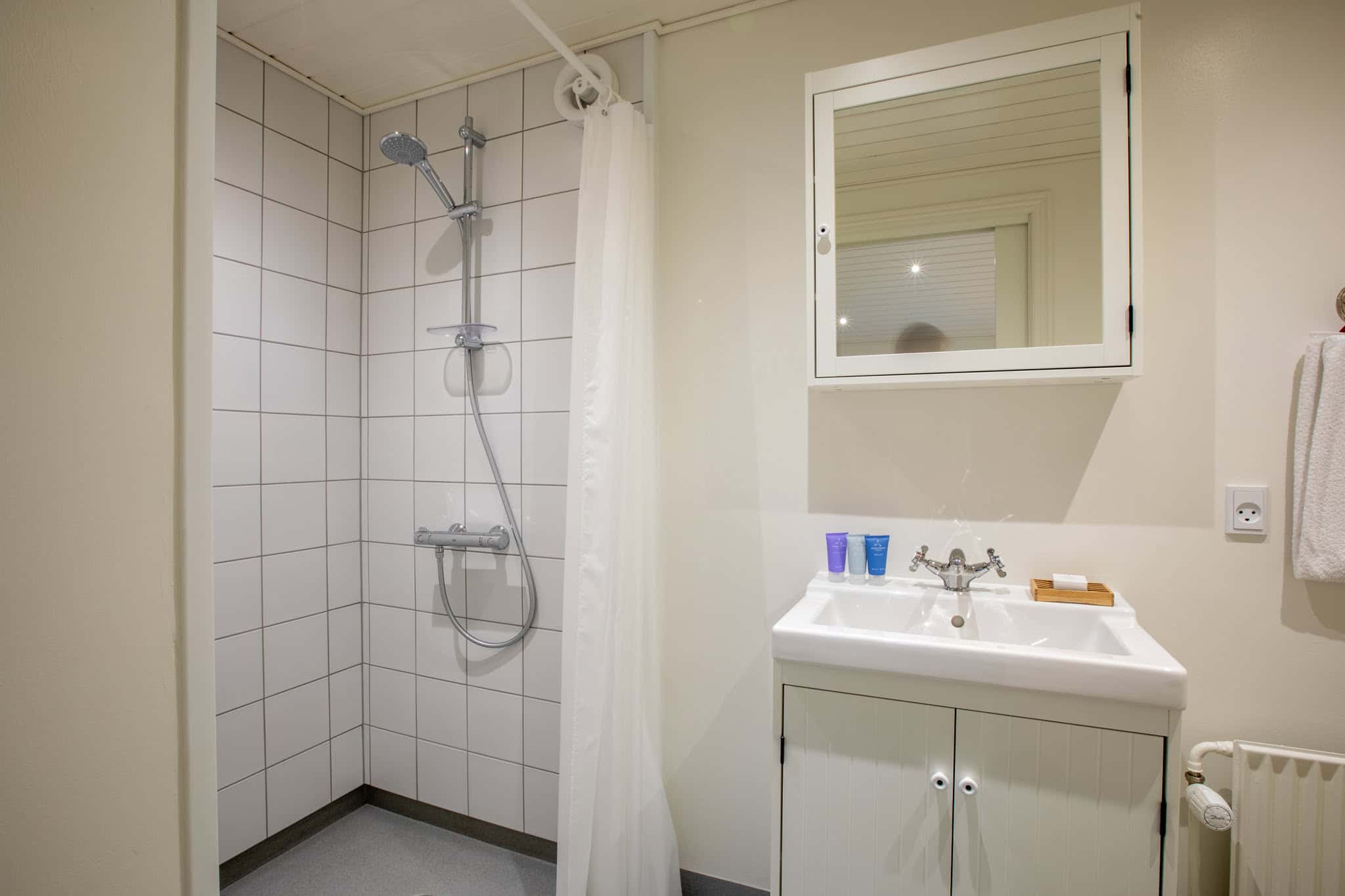 Rengøringsvenligt badeværelsesbadehotel med bruseniche og spejlskab på Knudhule Badehotel.