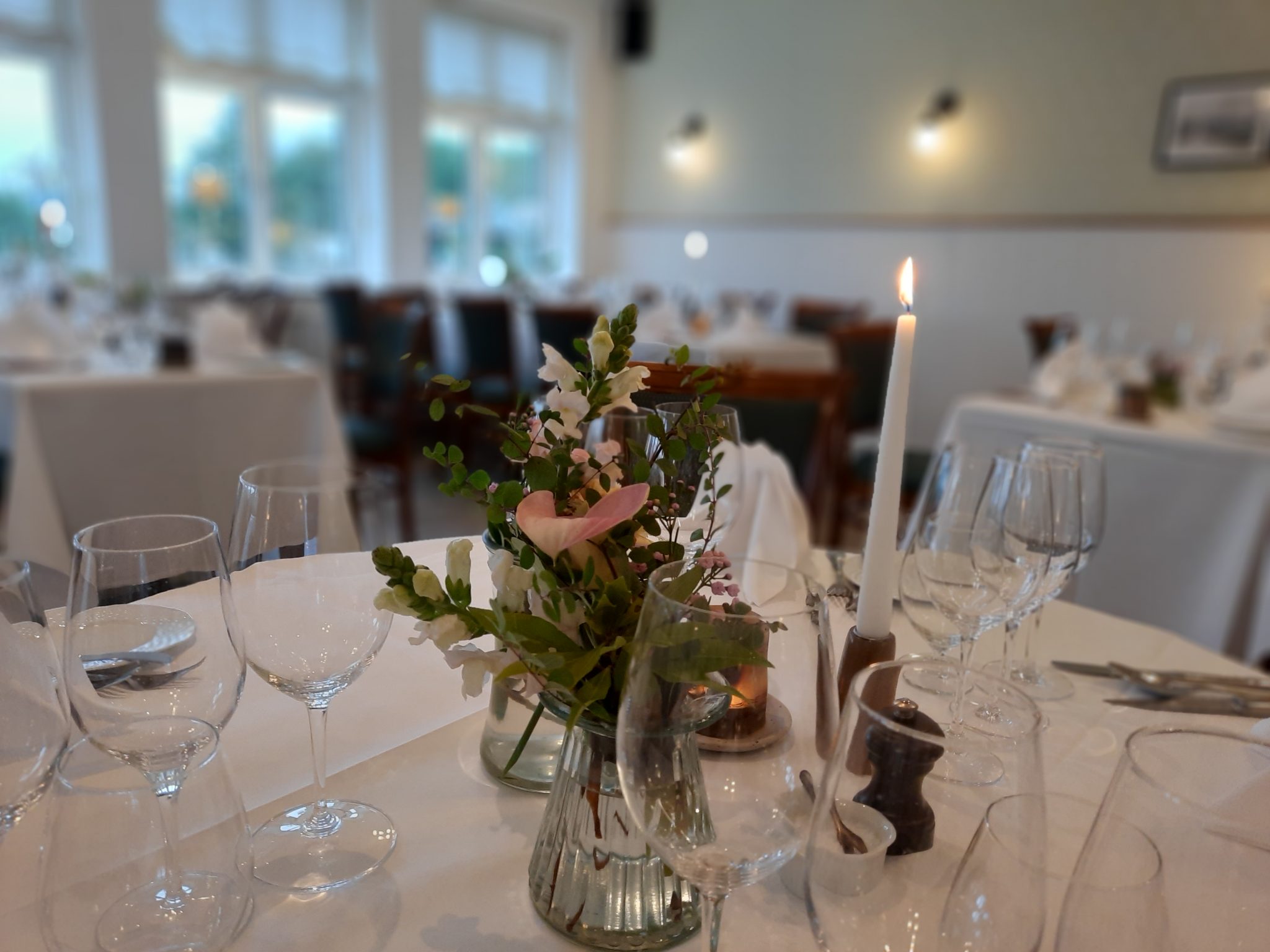 Elegant middagsborde med blomsterdekoration og stearinlys på Knudhule Badehotel.