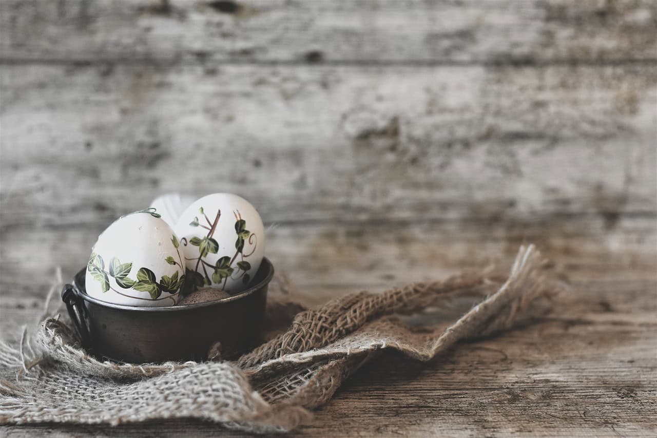 Æg med grønne blade-mønstre i sort skål på groft, rustikt træbord.