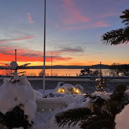 Fredeligt vinterudsigt ved Knudhule Badehotel med sneklædte grantræer og solnedgang over vandet.