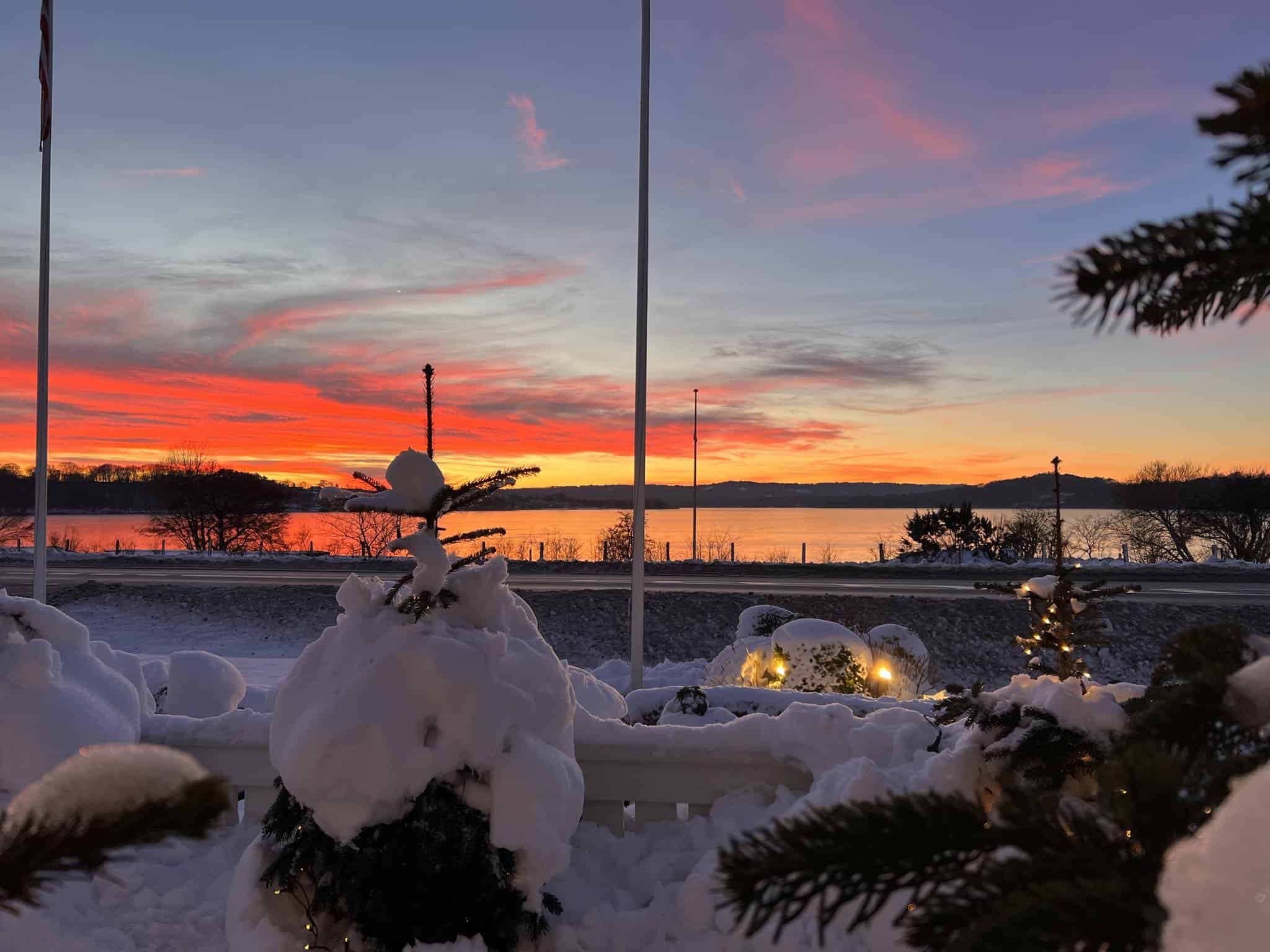 Fredeligt vinterudsigt ved Knudhule Badehotel med sneklædte grantræer og solnedgang over vandet.