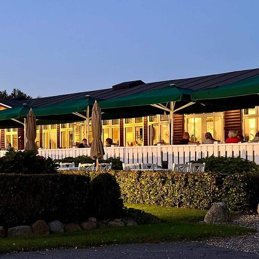 Udsigt over Knudhule Badehotel med hyggelig udendørs spiseområde i aftenbelysning.