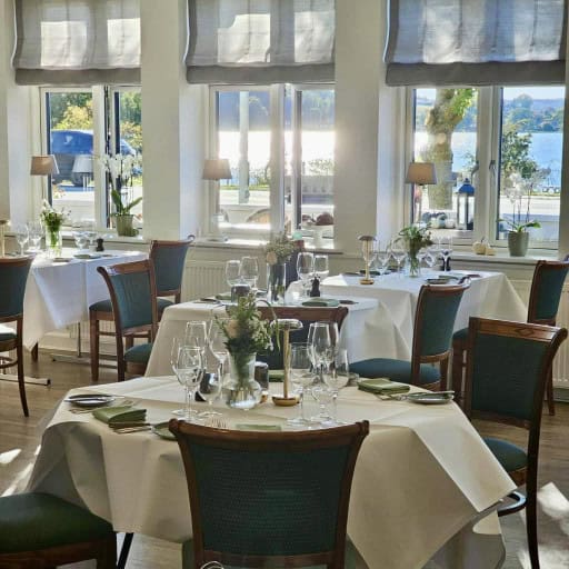 Elegant indendørs restaurant med udsigt over vand, flotte blomsterdekorationer og stilfuldt spiseområde på Knudhule Badehotel.