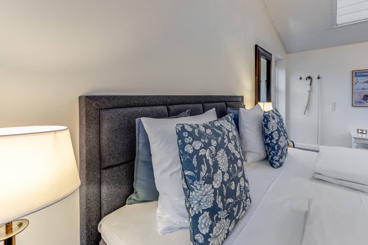 Blødt hotelværelses seng med blå blomsterpudes og behageligt lys fra lamper, perfekt til afslapning.