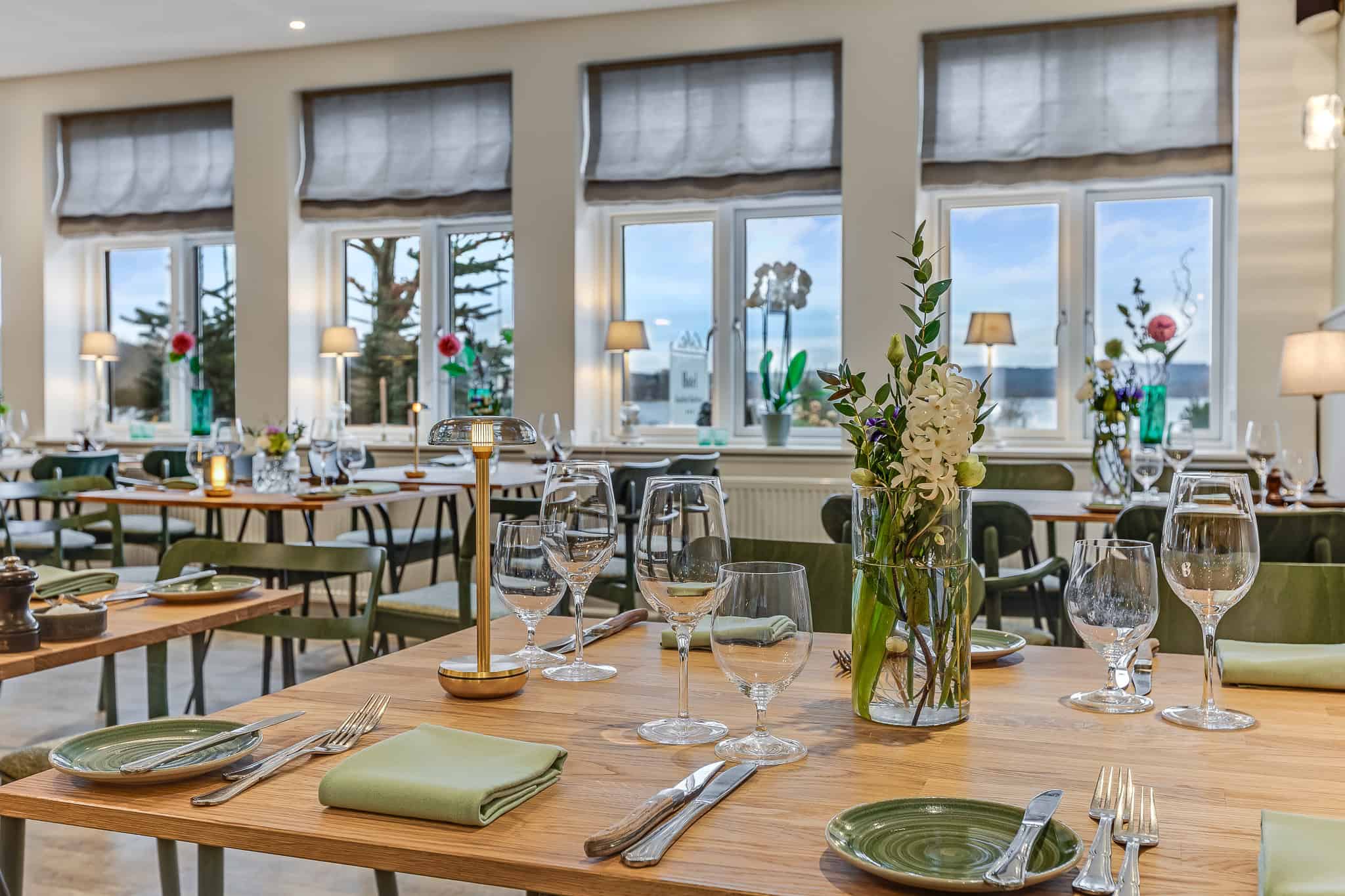 Rummelig restaurant med store vinduer, blomsterdekorationer og elegant borddækning på Knudhule Badehotel.
