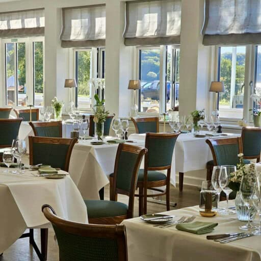 Indendørs restaurant med store vinduer og elegant borddækning.