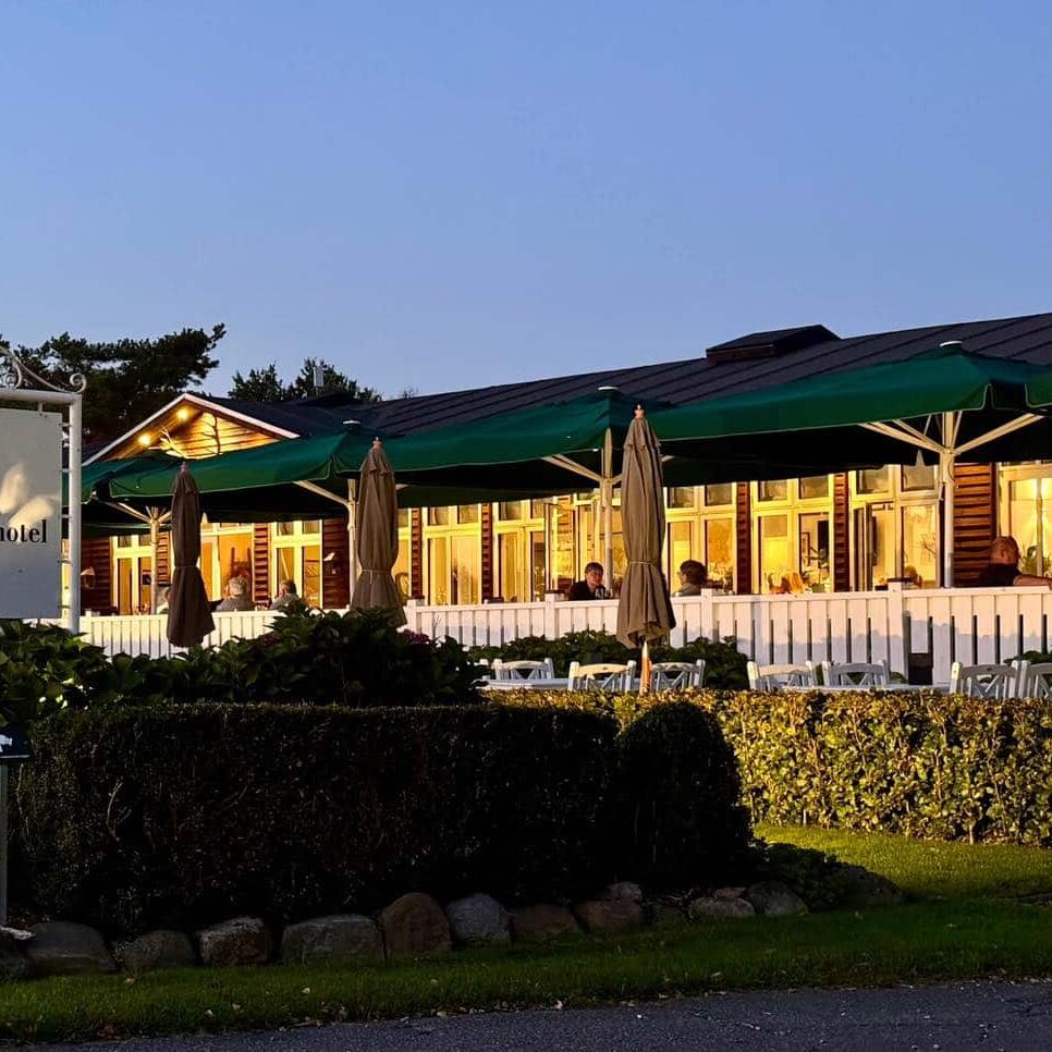 Udsigt over Knudhule Badehotel med hyggelig udendørs spiseområde i aftenbelysning.