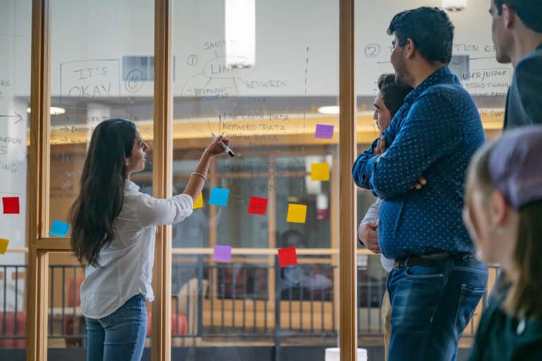 A classroom session where they are using glass walls as a white board to brainstorm ideas.