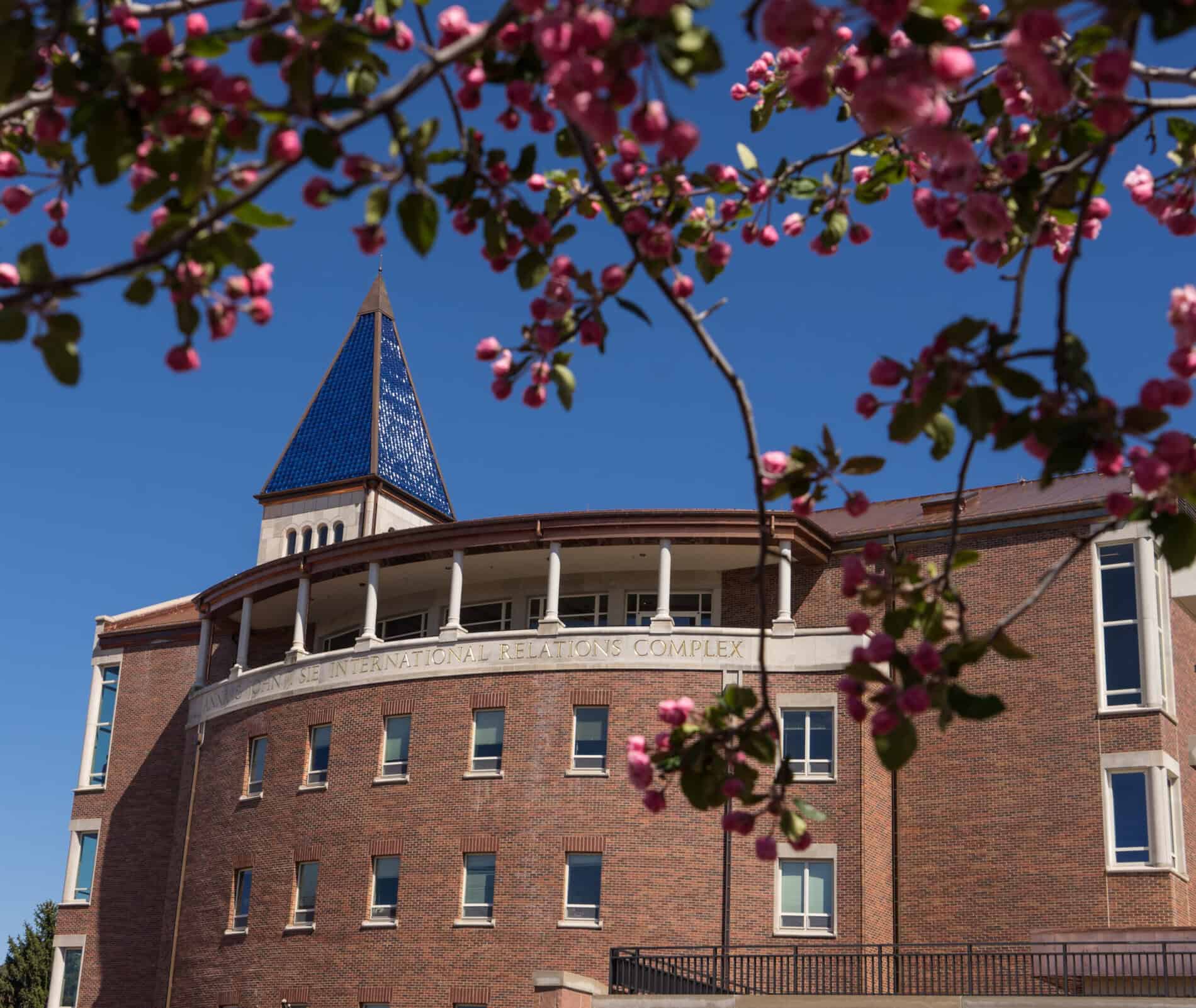 Exterior of the Sie International Relations Complex featuring the blue spire and a tree with blooming flowers.