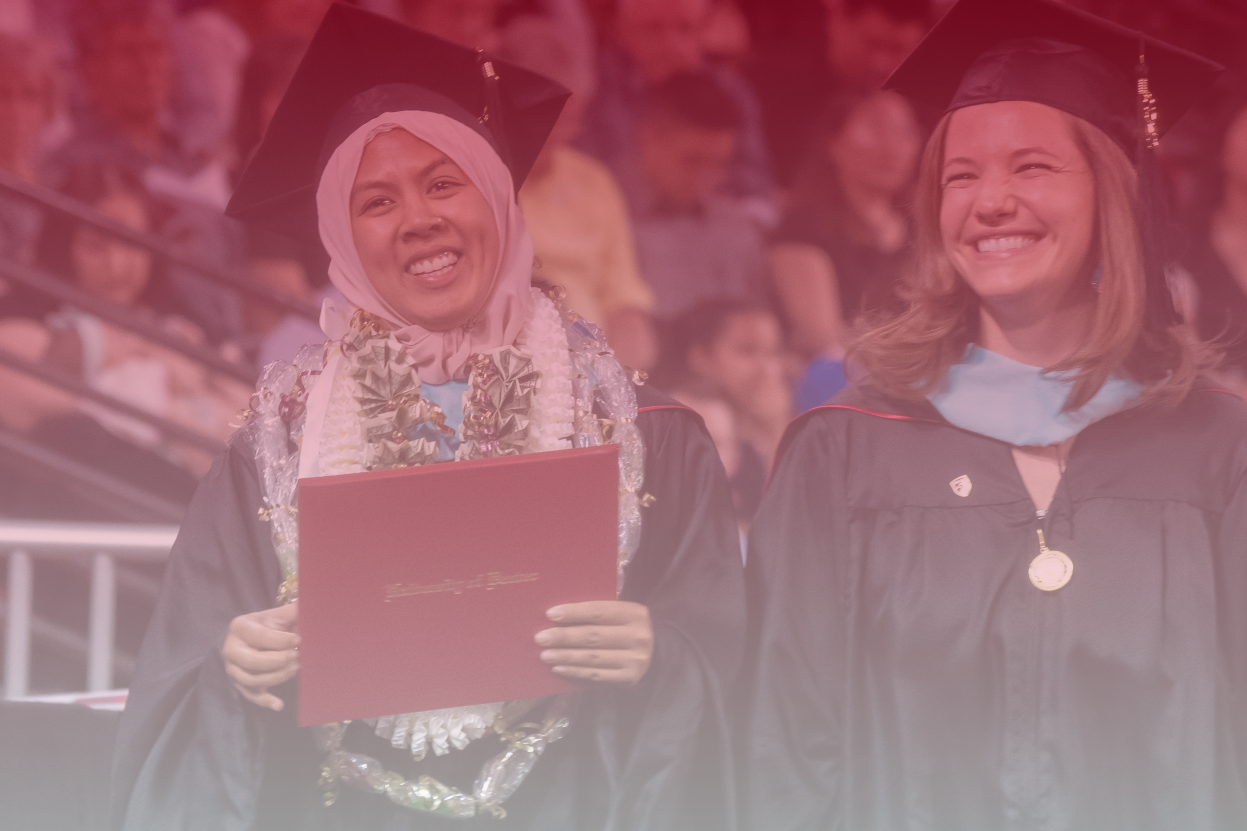 Two students at the graduate ceremony with one holding their degree.