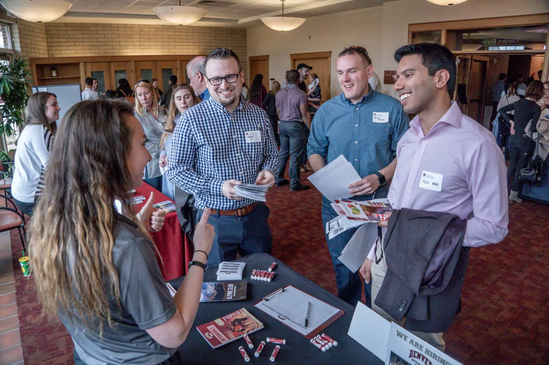 Three newly admitted graduate students talking to a Denver University representative at a table.