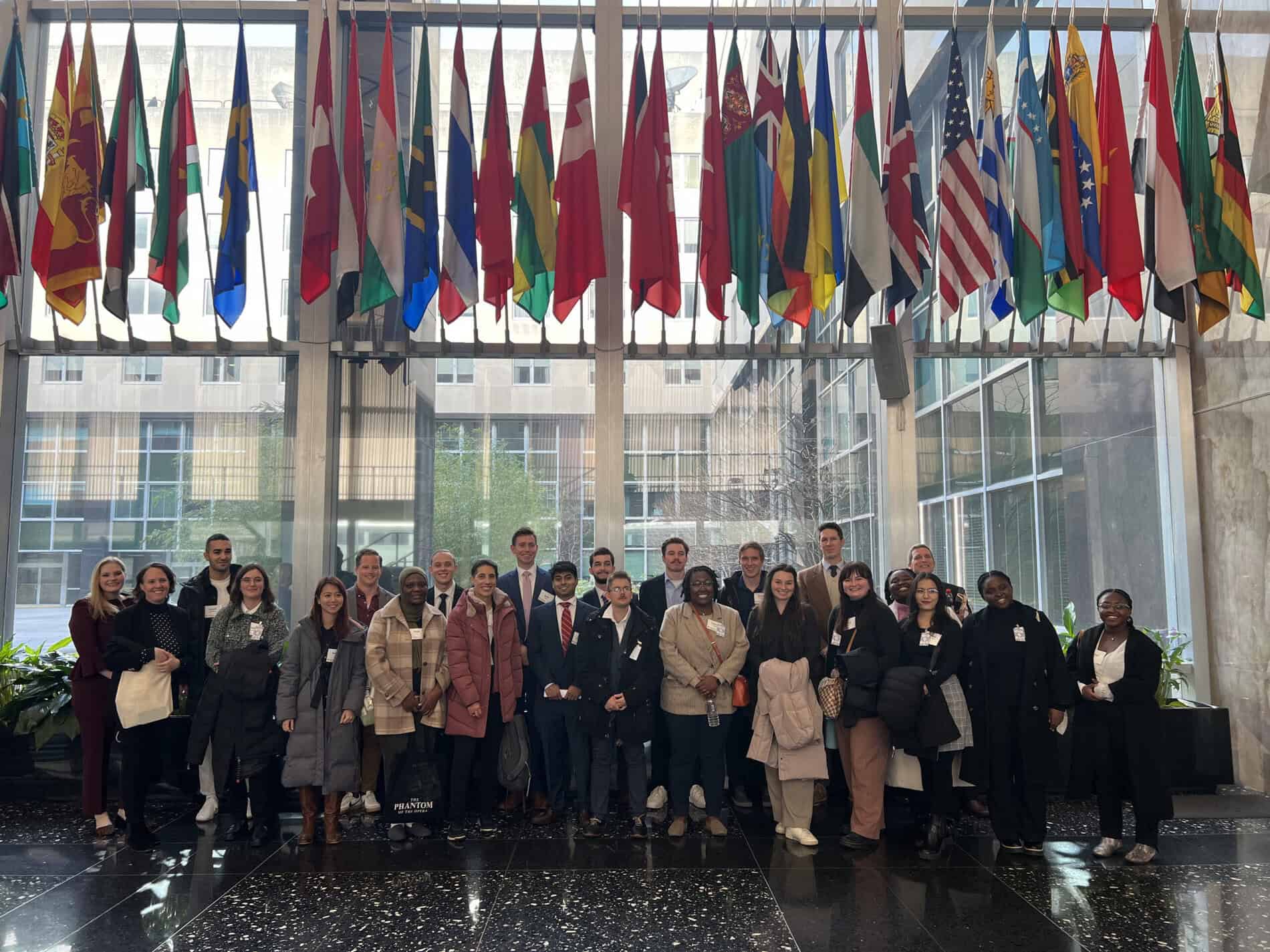 Group of students standing in front of a window with flags from various countries.