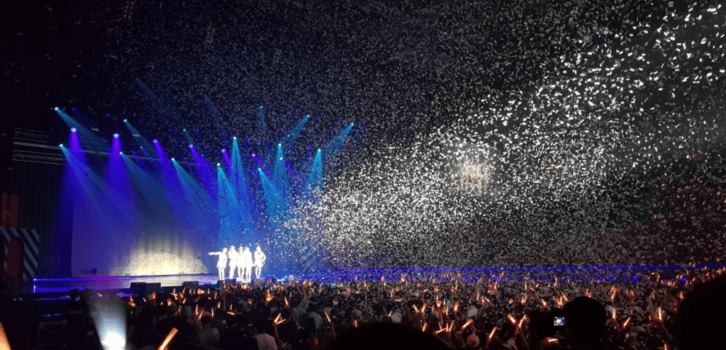 A concert audience holding glowing K-Pop lightsticks in unison.
