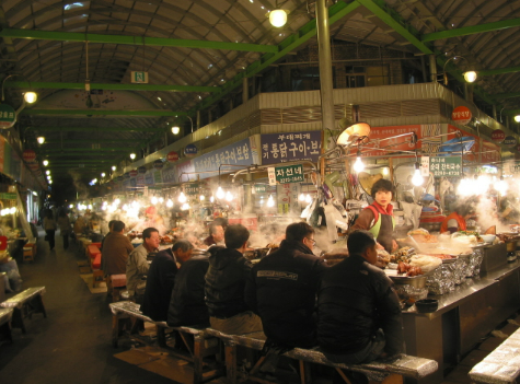 Gwangjang Market food stalls with people eating bindaetteok and kimbap.