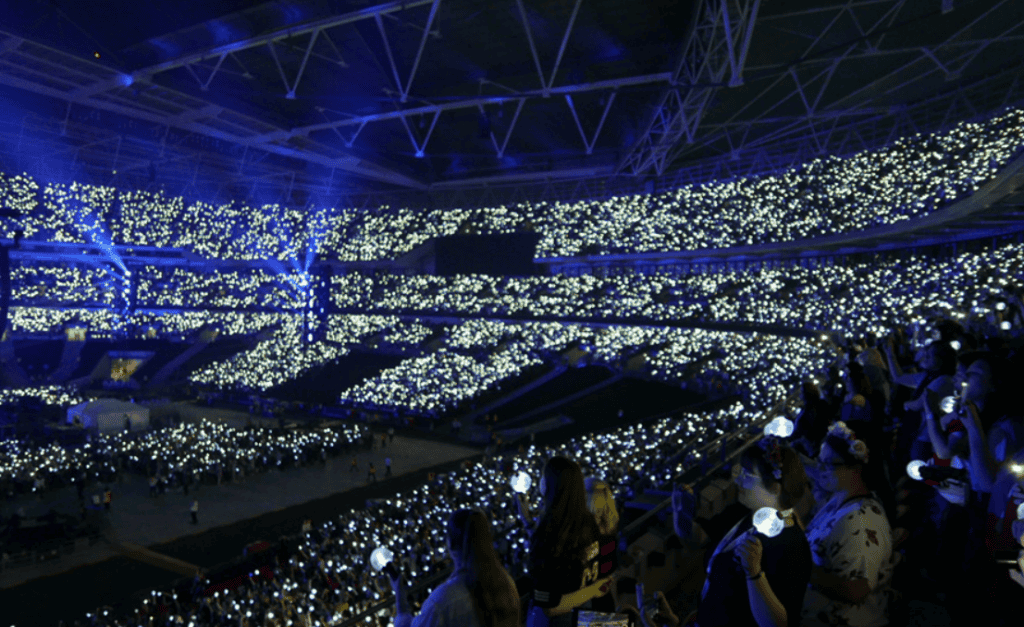 K-Pop concert with fans holding light sticks.