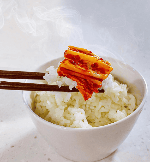 A bowl of steamed rice with kimchi on the side.