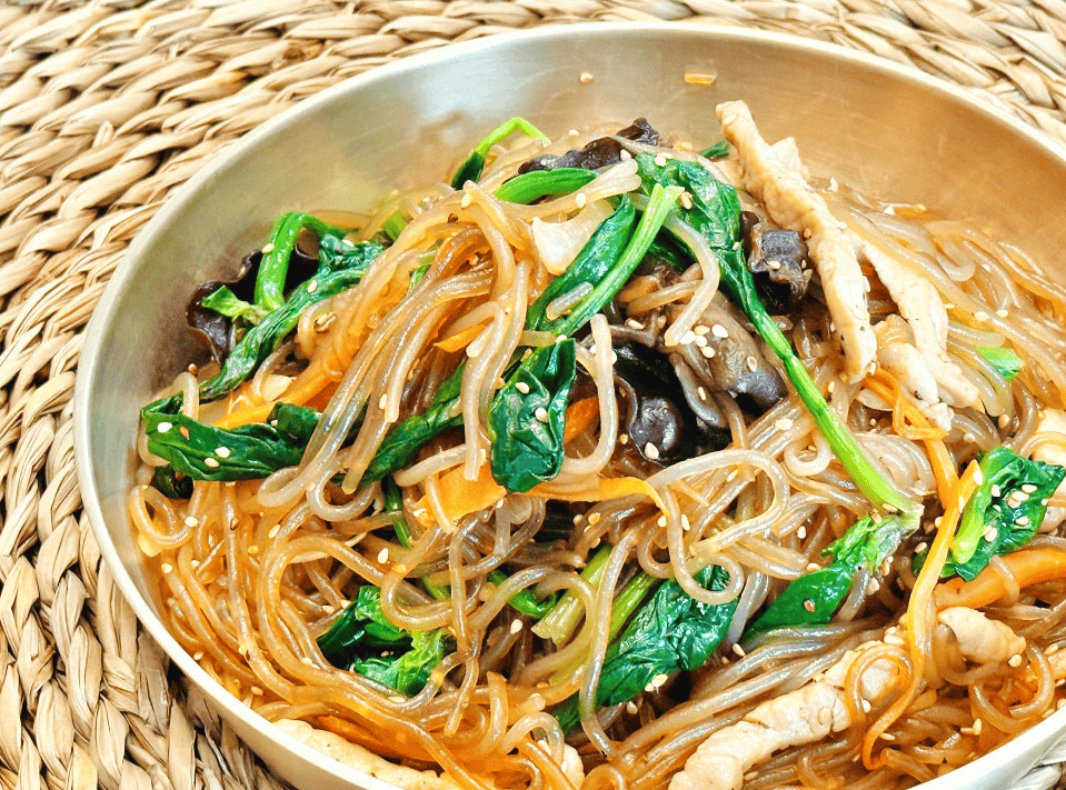 A bowl of Korean japchae noodles with vegetables and beef.