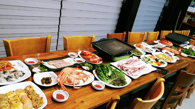 A Korean BBQ table setup with grilled meat, lettuce wraps, and side dishes.