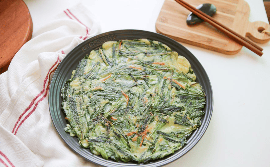 A Korean green onion pancake sliced on a plate with dipping sauce.