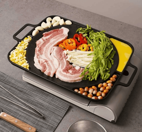A tabletop grill pan with pork belly slices and garlic.