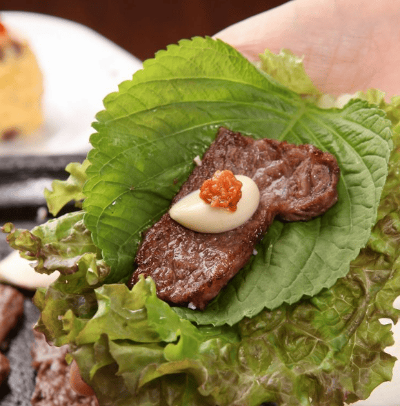 A Korean lettuce wrap filled with grilled meat, rice, and sauce.