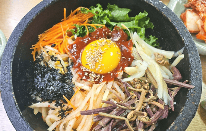 A vibrant bowl of Korean bibimbap with vegetables, beef, and fried egg.