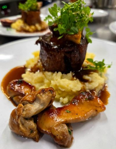 Primer plano de pies de cerdo deshuesados y rellenos, servidos sobre parmentier y bañados en salsa demi-glace con guarnición de ceps confitados en KRAM.