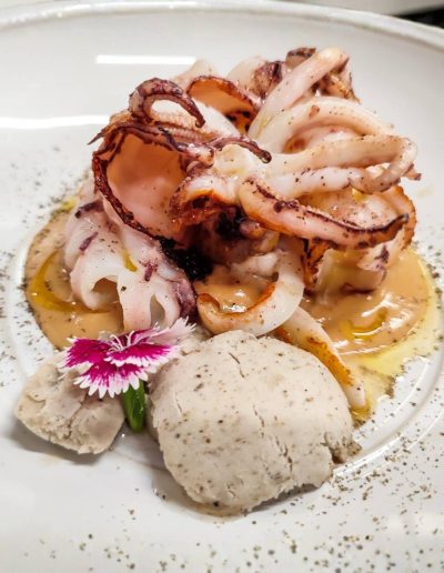 Emplatado de lujo de calamarcitos de playa frescos, salteados y servidos sobre una base de salsa cremosa y esferas de puré en KRAM.