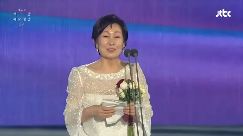 Kim Hye-ja holding a piece of paper and flowers onstage