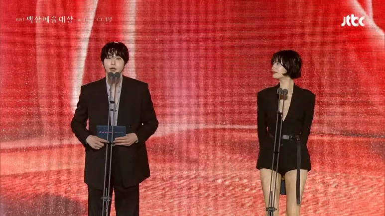 Nana in a belted black romper beside another awards presenter